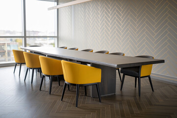 Long wooden table with yellow and dark gray chairs in a modern office, showcasing a sleek and professional workspace near a window