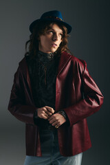 Young man exudes charm in stylish leather jacket and unique hat during urban photoshoot