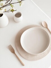 Table setting with a white tablecloth and a beige placemat. on the table, there is a white plate, a wooden spoon, and a wooden fork.