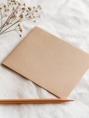Flat lay of a beige-colored notebook and a wooden pencil on a white textured surface. the notebook is open and the pencil is resting on top of it.
