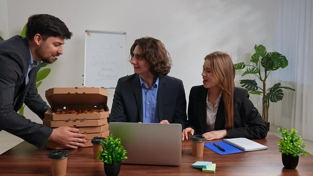 Business team of men and woman working at desk in the office having dinner break with food delivery, man brings stack of pizza boxes, team taking out slices. Slow motion.