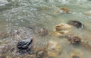 Obraz premium mountain river flowing over assorted rocks. soft water movement with shimmering reflection. natural texture. abstract nature background, nature design, eco