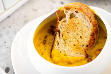 A bowl of vibrant orange pumpkin soup paired with golden crusty bread, showcasing an appetizing, cozy meal in a rustic setting. Perfect for autumn and food styling.