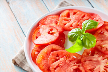 White Plate with Tomato Slices and Basil Leaves on Rustic Wooden Table, Close-Up