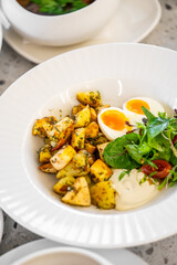 Fresh and colorful meal featuring roasted potatoes, a halved soft-boiled egg, cherry tomatoes, salad greens, and creamy sauce on a white plate. Perfect for healthy dining and gourmet photography.