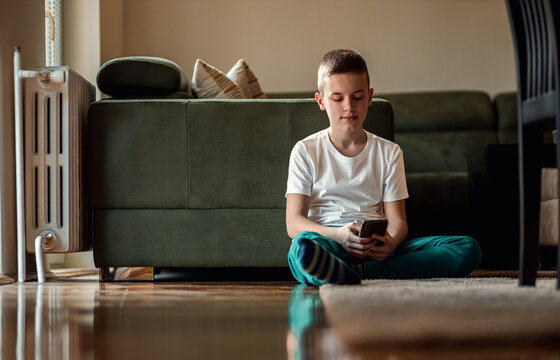 Boy sitting on floor at home using smart phone typing message to a friend.