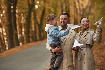 Fototapeta premium With paper planes. Happy family are together in the autumn forest near the road