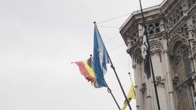 Bandiera Belga e bandiera Europea, riprese dal basso, durante una giornata nuvolosa. Citt&agrave; Europea