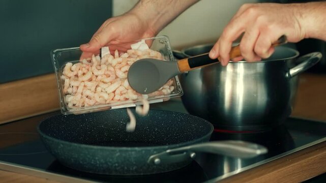 Adding shrimp from plastic container into frying pan. Pouring thawed seafood onto heated skillet. Transferring pink prawns into non stick pan for cooking. Dropping defrosted shellfish onto preheated