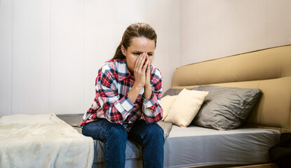 Obraz premium Stressed woman sitting on bed in bedroom covering face with hands