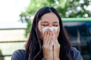 Woman suffering from seasonal allergies, holding a tissue to her nose. Hay fever, pollen allergy,...