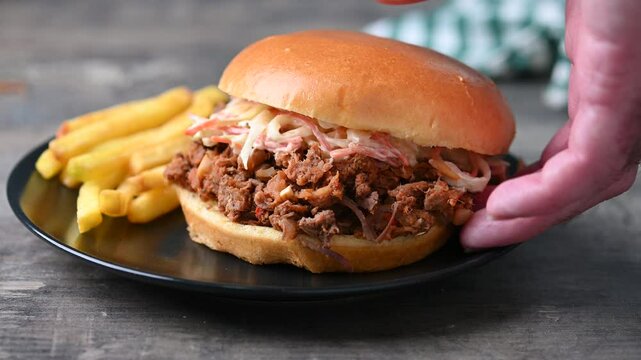 Pulled pork sandwich with coleslaw salad and french fries on wooden table