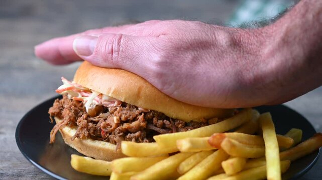 Pulled pork sandwich with coleslaw salad and french fries on wooden table