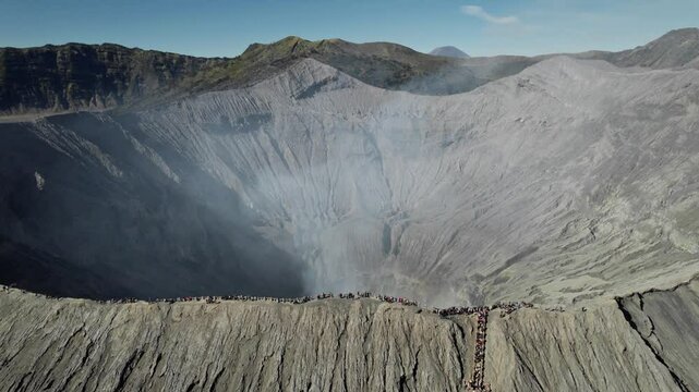 Drone view of mount bromo crater emitting smoke with tourists watching