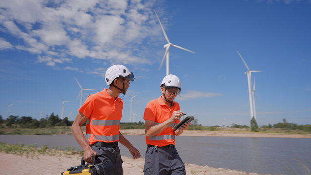 In a wind farm, two Asian inspectors are walking around the turbines, examining the work areas for potential impacts on the surrounding community. Engineer Wind Turbine.