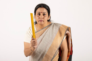Portrait of an indian school teacher scolding with holding scale on white studio background