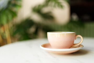 pink cup with small plate with cappuccino coffee on white table at sunny work day