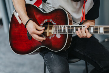 A close-up view of a person skillfully playing a red acoustic guitar, capturing the artistic expression and dedication of music creation in a contemporary indoor setting.