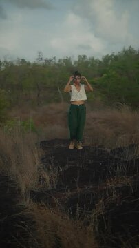 Indian woman in green pants and a crop top walks across a charred, dry forest area. India