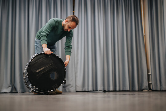 A person working with a bass drum in a well-lit studio. The image showcases musical preparation, depicting the process and focus required for excellent performances.