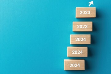 Wooden Blocks Stacked with Years 2023 and 2024 with Arrow on Teal Background Symbolizing Future Planning