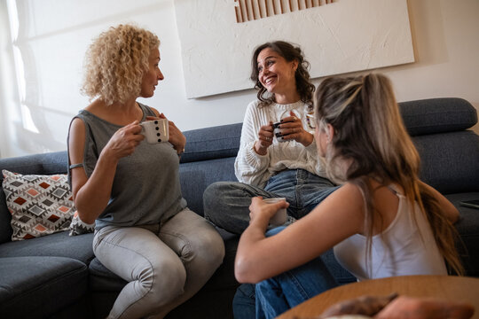 A modern mother enjoys a coffee while spending time with her two daughters. They sit together in living room, talking and sharing laughter.	