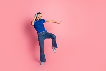 Young woman happily enjoying music with headphones while dancing against a pink background wearing a blue polo shirt