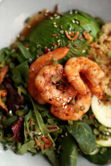 Bowl with quinoa, shrimp, avocado, greens, arugula and cucumber close-up