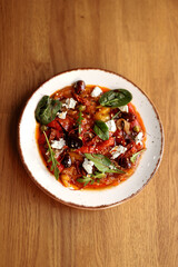 Marinated peppers with feta cheese, olives, capers and basil on a white plate