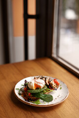 Toasted bread sandwich with guacamole, red fish, egg and greens on a plate on a brown table