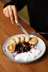A girl cuts Round Cottage cheese pancakes on a plate with butter cream and cherry jam