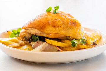 roasted chicken thigh with potatoes, lemons, and shallot onions in a dish close-up