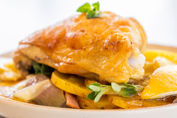 roasted chicken thigh with potatoes, lemons, and shallot onions in a dish close-up