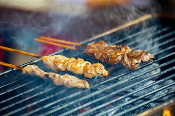 several meat skewers sizzle on the charcoal grill