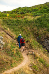 Obraz premium Senior couple (back view) hiking in in summer at picturesque hills in Emerald Coast, Brittany, France. Healthy, active lifestyle, elderly wellbeing concepts. French countryside tourism background.