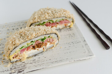 Sushi burger with tuna, cucumber, onion, cheese and rice in a nori with a crispy crust on a white plate with chopsticks. Hybrid food concept. Horizontal orientation. Selective focus.