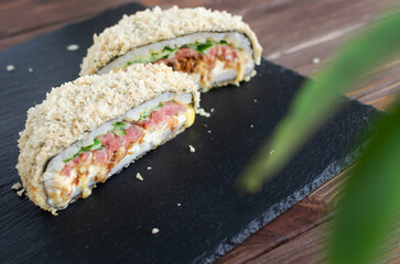 Sushi burger with tuna, cucumber, onion, cheese and rice in nori with crispy crust on a black plate on a wooden table. Creative dish. Hybrid food concept. Horizontal orientation. Selective focus.
