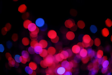 Blurred red, purple and blue lights create a beautiful bokeh effect on a black backdrop, evoking a festive and dreamy atmosphere.