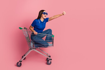 Young Woman Sitting in Shopping Cart Posing Enthusiastically On a Vibrant Pink Background