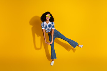Smiling stylish young woman posing in vibrant yellow background showcasing casual fashion and...
