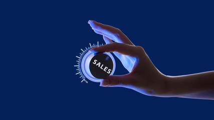 Hand adjusting glowing dial labeled SALES against blue background. Control and potential for...