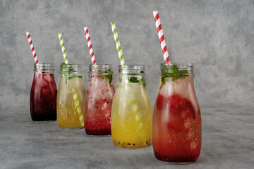 Five glasses of refreshing lemonades with different flavors on a light gray background. Lemonade with strawberries, mango, currants, raspberries in a glass . Concept of trendy cold drinks .