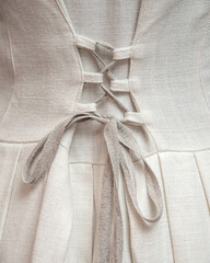 White linen dress abstract, back corset binder, grey lace. Traditional beautiful dress for ethnic wedding. Organic cloth texture, light background. Lady waist close up.