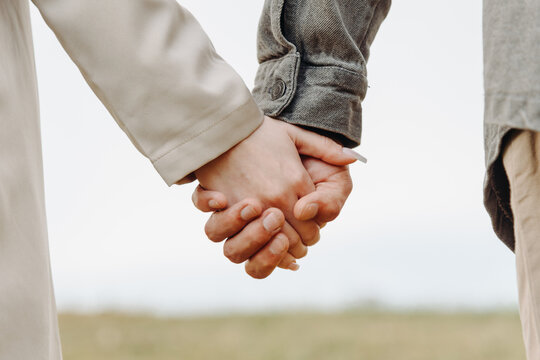 close-up view of couple holding hands, young beautiful caucasian man and woman take each other hands, walking on pathway in park in summer at sunset, love and family concept, selective focus