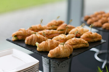 On the table, there is a tray filled with croissants and sandwiches