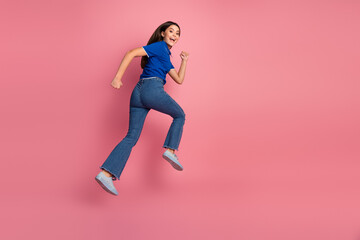 Smiling young girl joyfully jumping on pink background wearing casual blue t-shirt and jeans