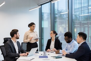 A diverse group of business professionals in a modern office setting collaborating during a meeting, using technology to discuss strategy.