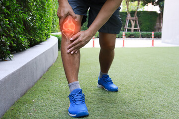 A man holding his knee which is sore from osteoarthritis while running outdoor.  OA knee symptom