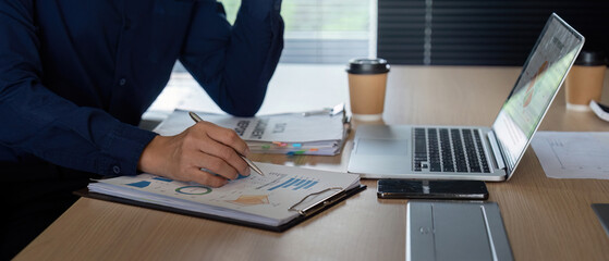 Data Analysis and Reporting. A focused professional taking notes and reviewing financial documents...