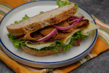 Plant based sandwich made with seitan, onion slices, vegan cheese, lettuce and seasoning